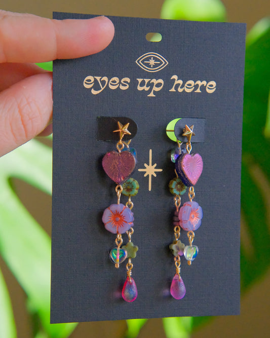 Colorful beaded earrings on a 'eyes up here' card with a blurred green plant background